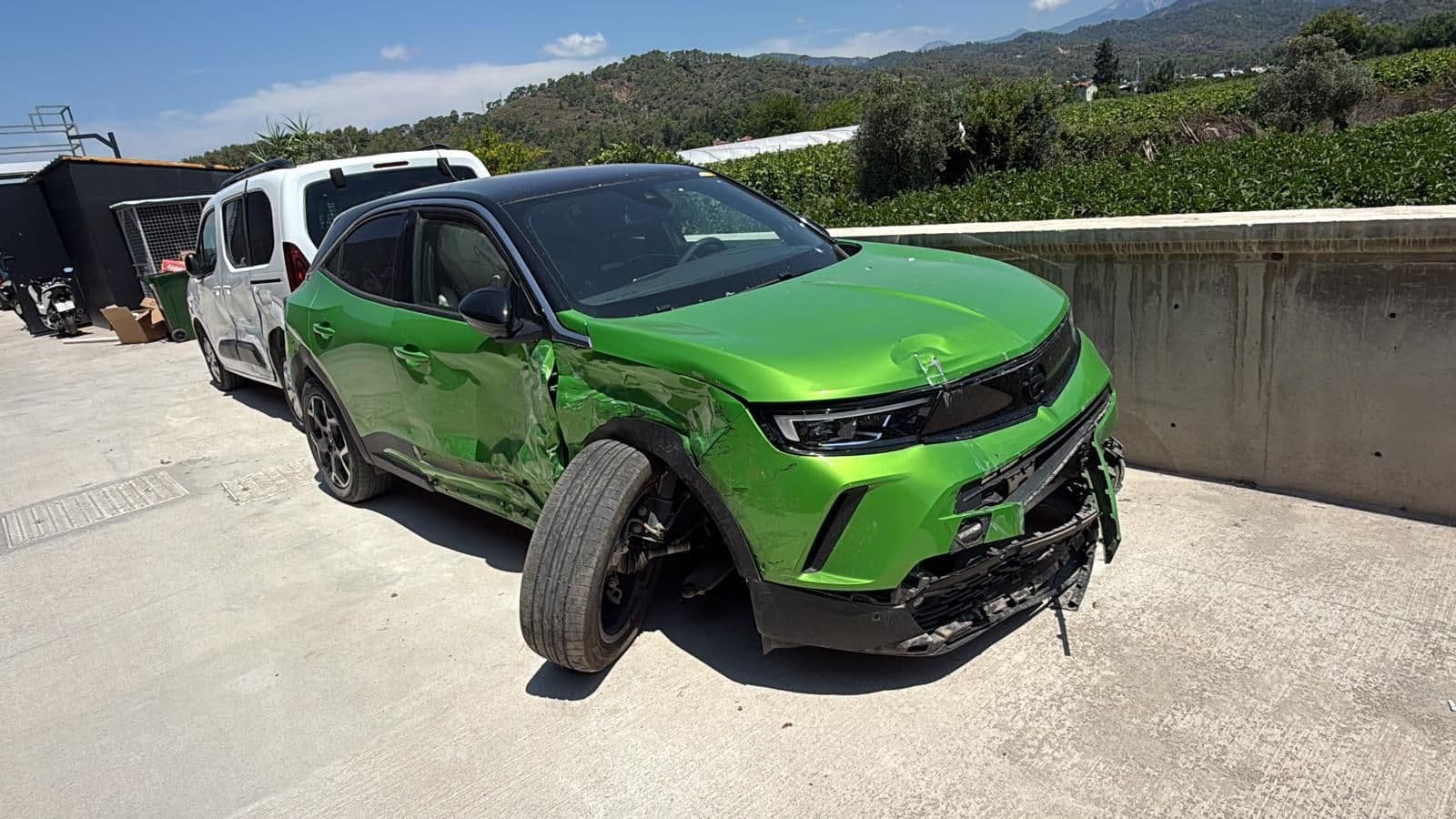 Ön sol tarafı hasarlı yeşil bir Opel Mokka; tampon kopmuş, ön teker yatmış